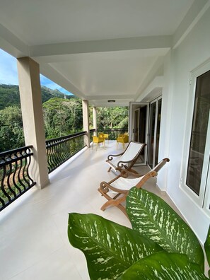 A balcony with two wooden lounge chairs and a table, overlooking a lush green landscape.