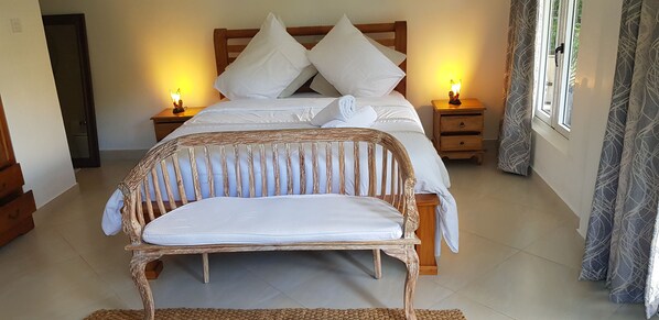 A bedroom with a bed, two bedside tables with lamps, a wooden chair, and a window with curtains.
