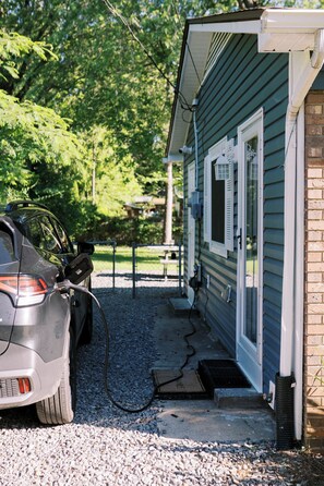 A car charging at a residential property with a gravel driveway, a wooden deck, and a brick wall.