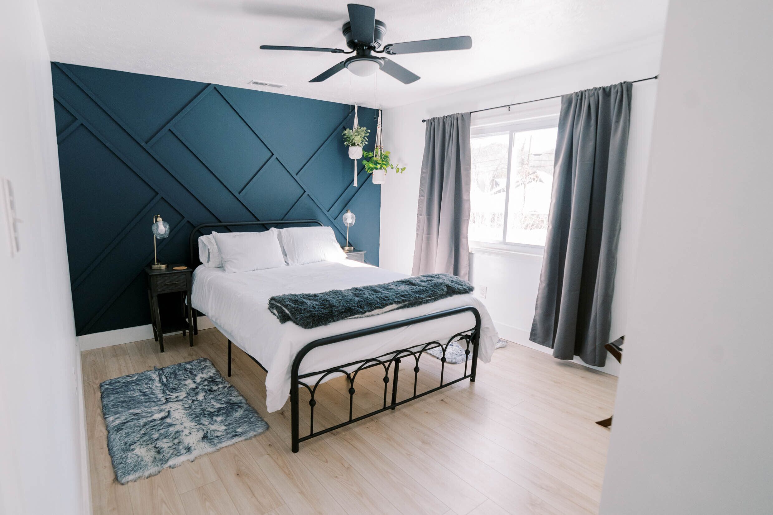 Un dormitorio moderno con cama, ventilador de techo, ventana con cortinas y planta en la pared.