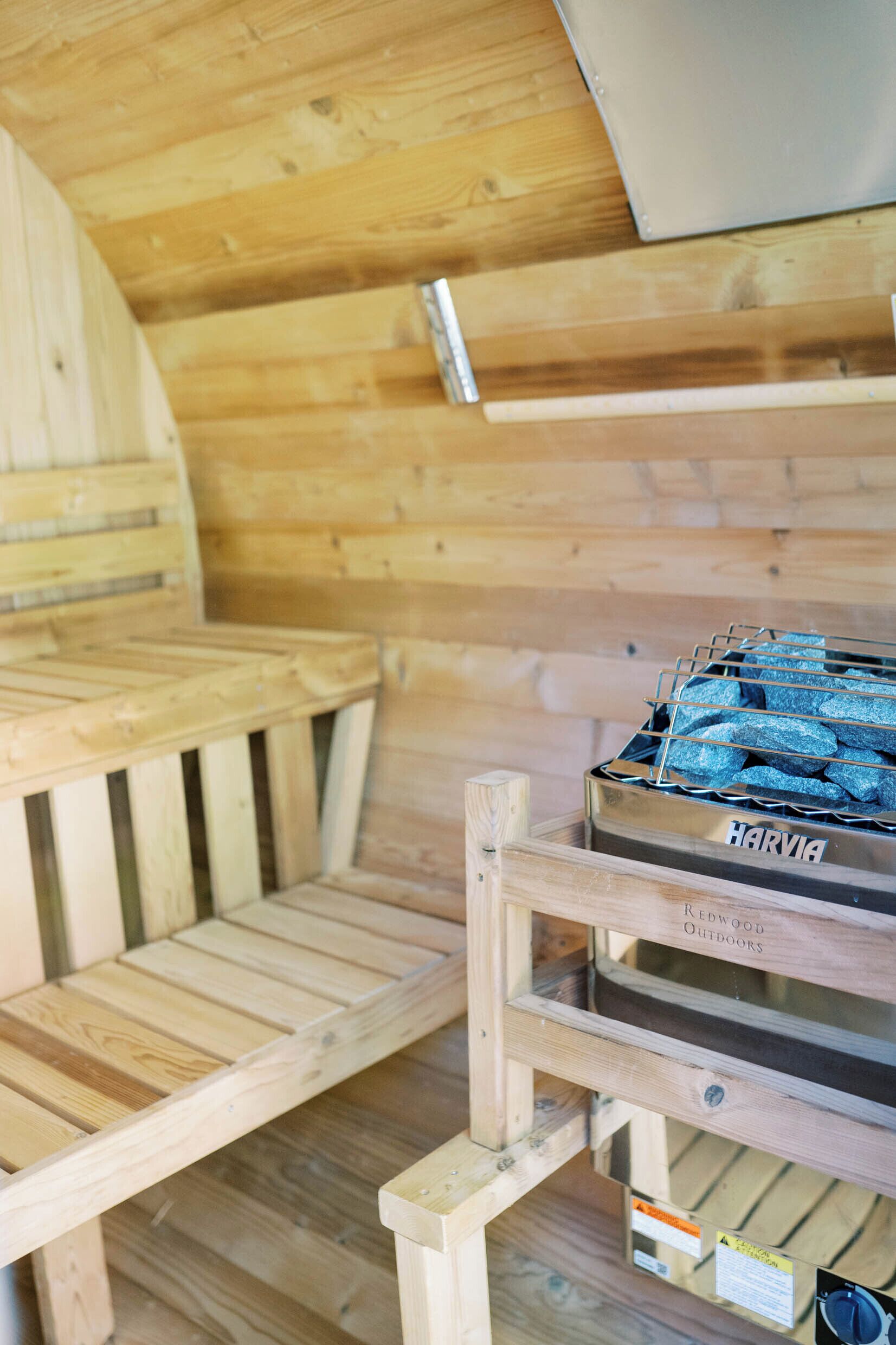 A sauna room with wooden benches and a metal container labeled "HARVIA" for stones.