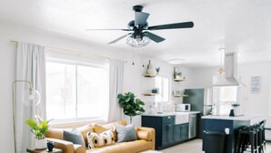 Een moderne woonkamer met een bank, salontafel en een eethoek met stoelen, met een keuken op de achtergrond.