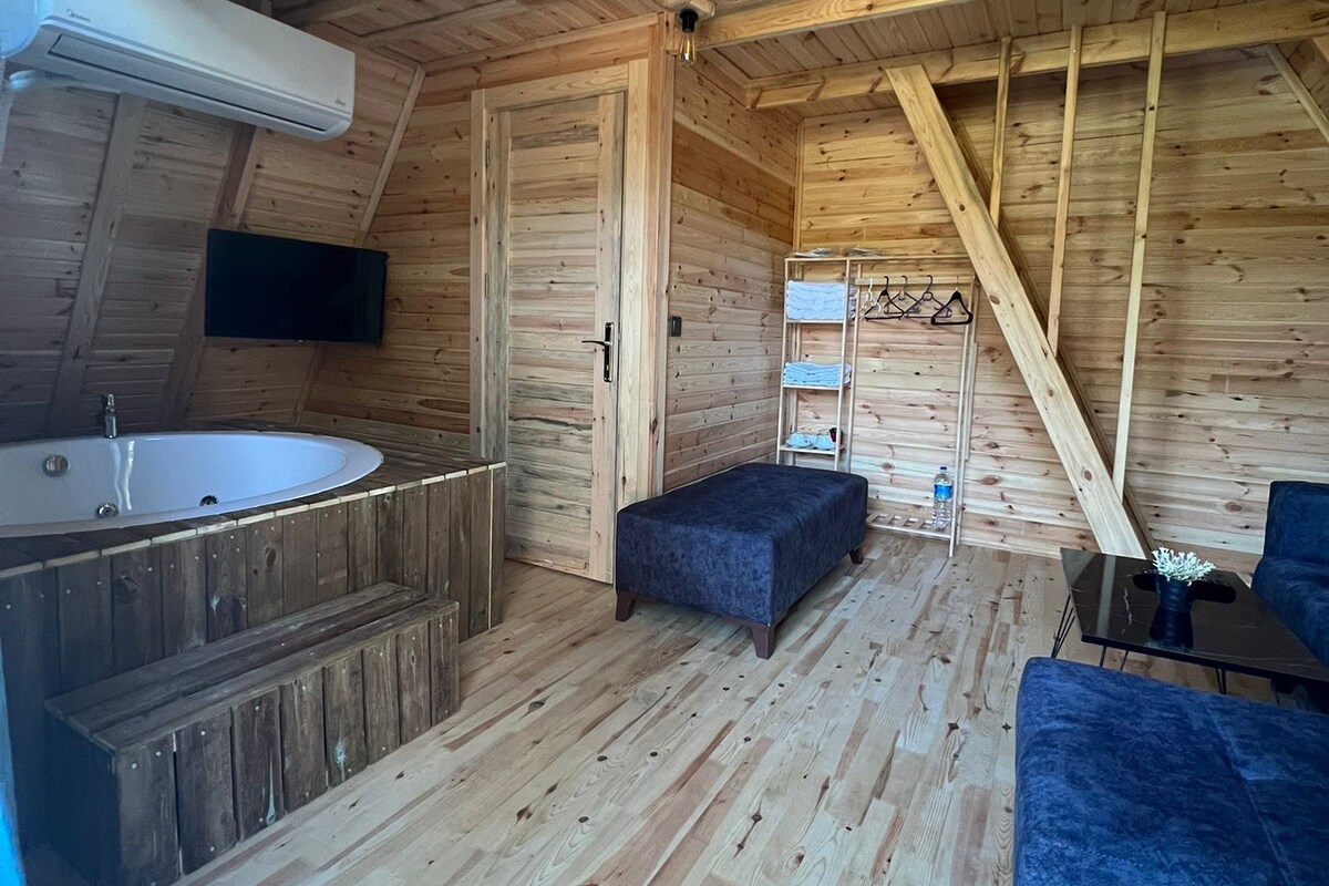 Een knus blokhutinterieur met houten vloer, een bubbelbad, een bank en een aan de muur bevestigde televisie.