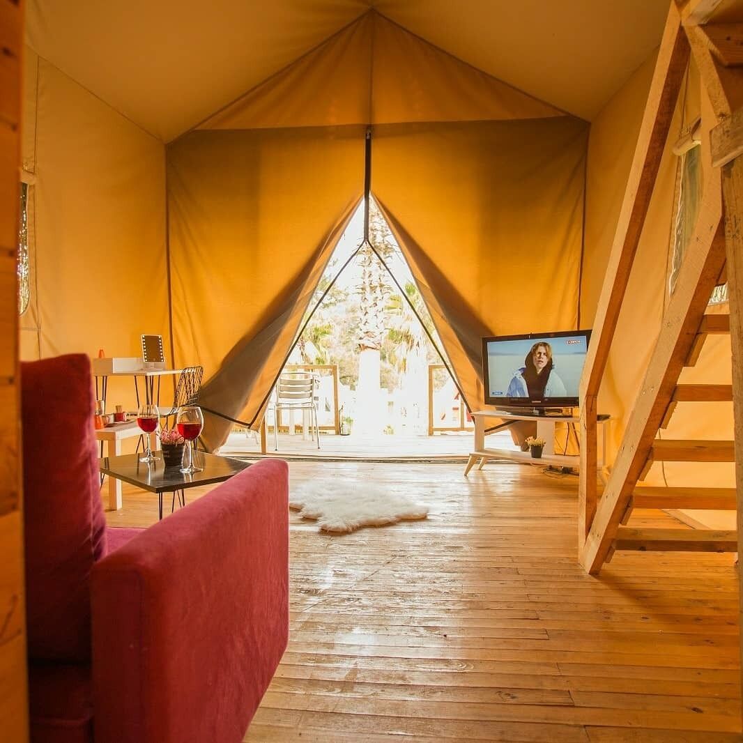 A tent with a television, a red chair, and a table with wine glasses.