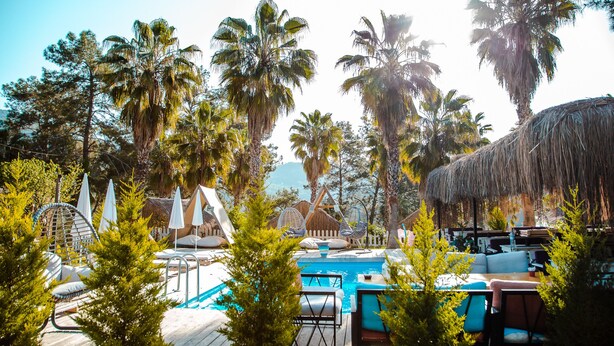 Un área de piscina con sillones de descanso, sombrillas y una estructura de techo de paja.