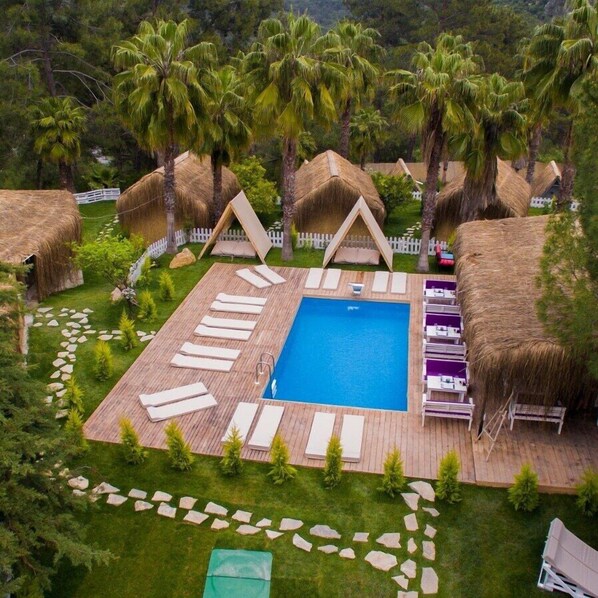 Zona de piscina con sillones de descanso, piscina y estructuras de techo de paja.