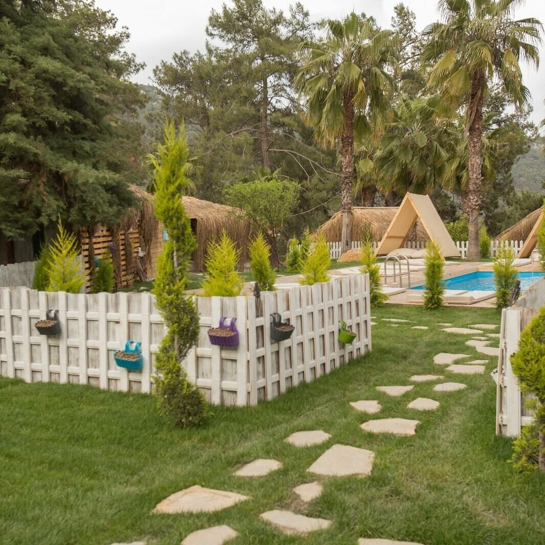 A backyard with a pool, palm trees, and a white fence with hanging planters.