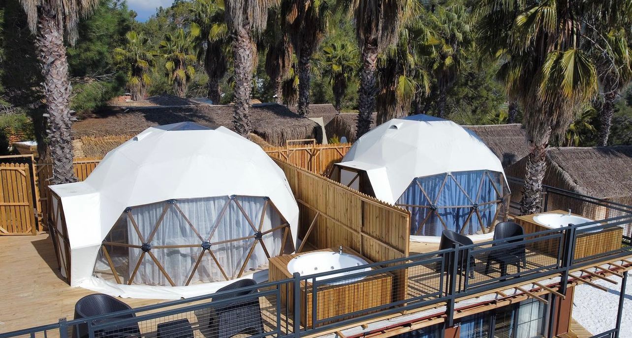 Dome-shaped tents with a wooden deck and thatched-roof structures in the background.