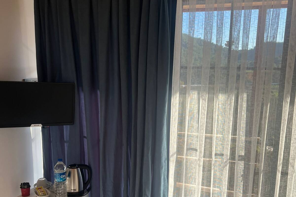 Ein Zimmer mit Holzboden, einem Flachbildfernseher, einem kleinen Tisch mit einer Wasserflasche, einem Wasserkocher und einer Fernbedienung.