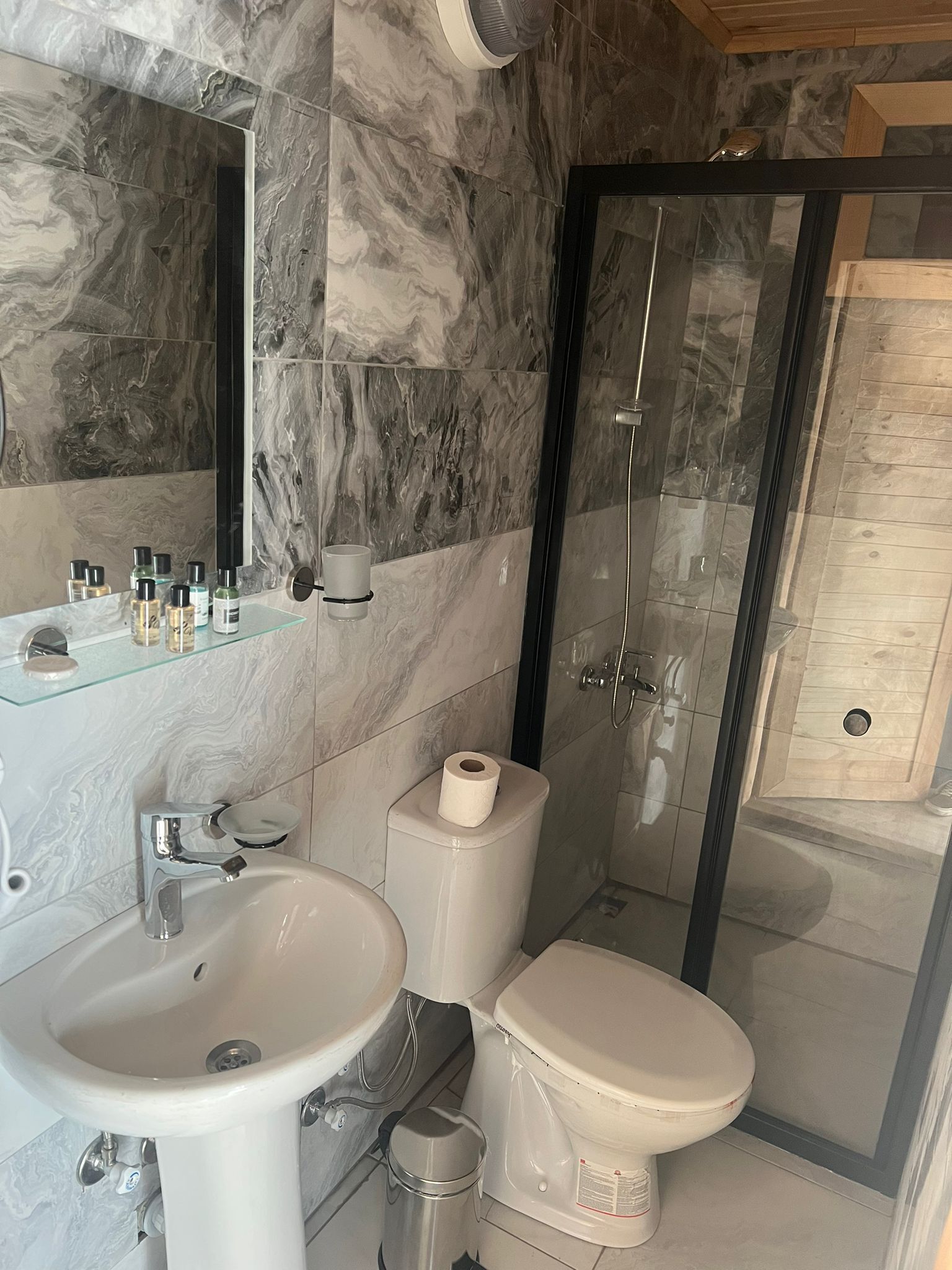Une salle de bain moderne avec un pare-baignoire en marbre, une douche en verre, un lavabo et des toilettes.