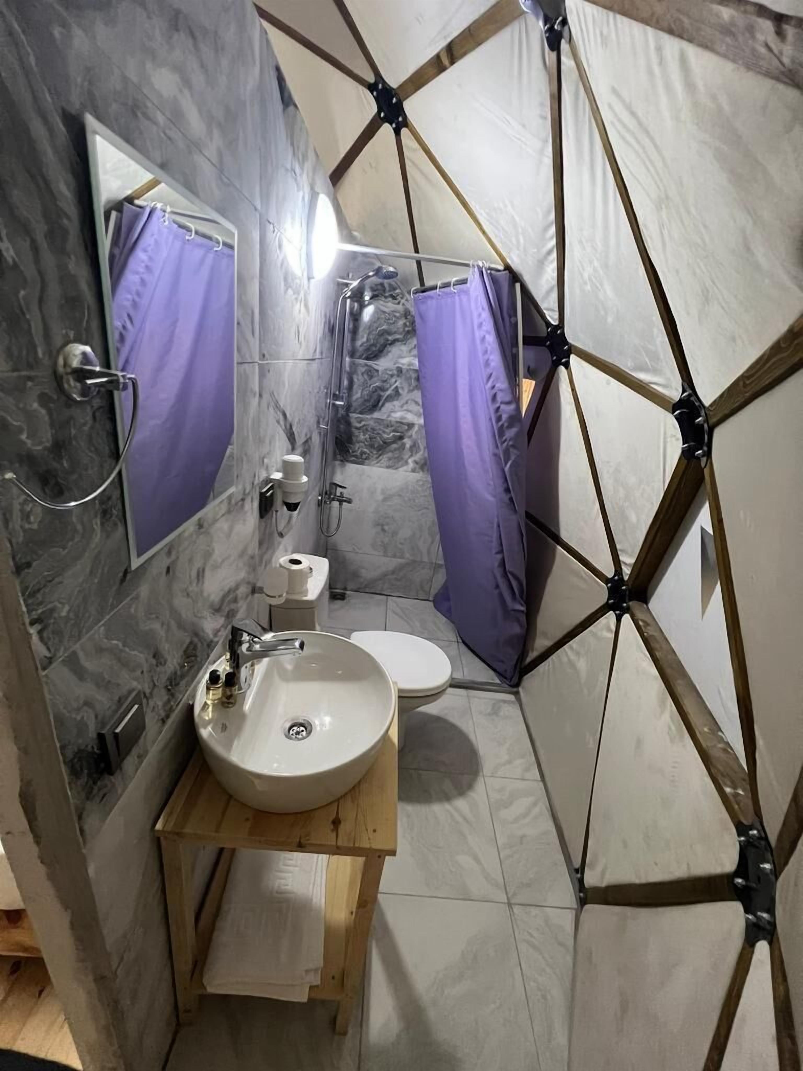 A bathroom with a marble wall, a sink, a toilet, and a shower area.