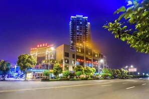 Un hotel de varios pisos con señalización iluminada, una entrada bien iluminada y un área de estacionamiento.