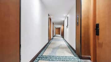 A hotel hallway with wooden doors, a patterned carpet, and framed pictures on the walls.