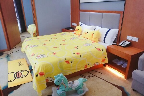 Quarto de hotel com uma cama coberta por um edredom com tema de patos amarelos, um pequeno cavalo de brinquedo, um pato de pelúcia e um telefone de mesa.