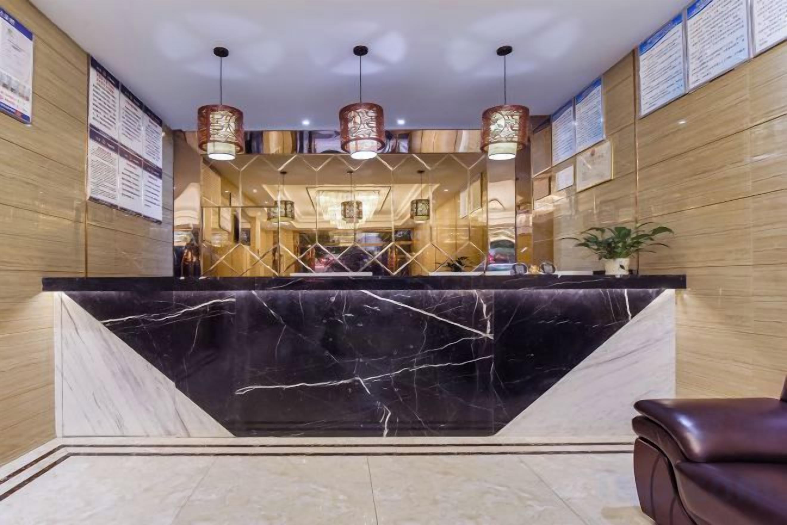 A hotel reception area with a marble counter, wooden paneling, and hanging lamps.