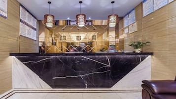 A hotel reception area with a marble counter, wooden paneling, and hanging lamps.