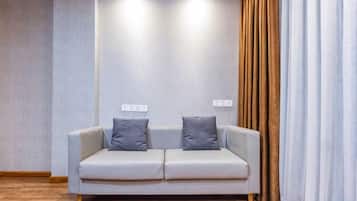 A room with a light-colored sofa, two pillows, a wooden floor, and a wall with a textured pattern.