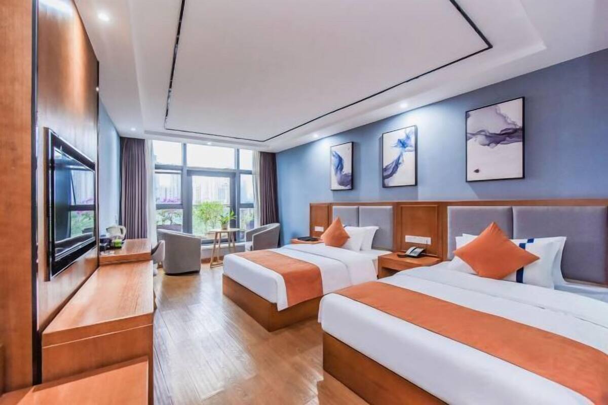 Une chambre d’hôtel avec deux lits, une télévision, un bureau et une grande fenêtre.