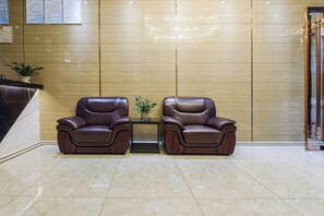 Un área de recepción con dos sillones de cuero, una mesita con una planta y una pared de madera con líneas verticales.