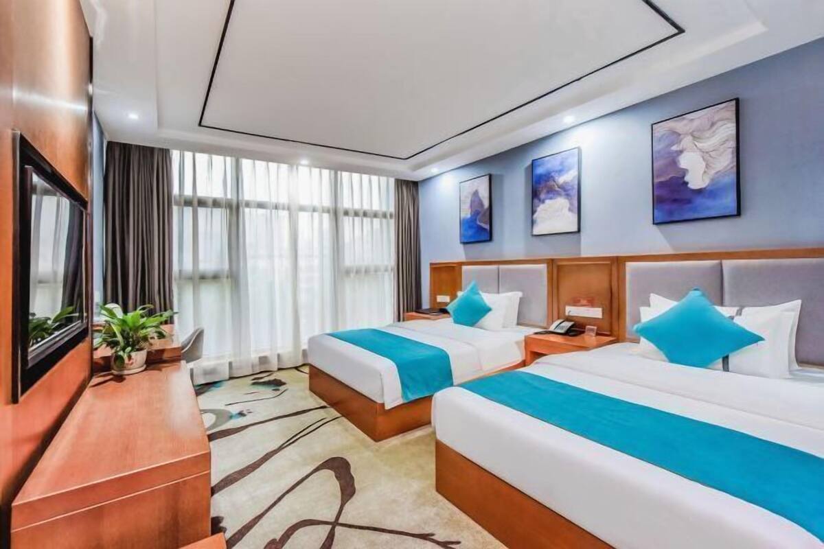 Une chambre d’hôtel avec deux lits, une télévision, un bureau et une grande fenêtre.