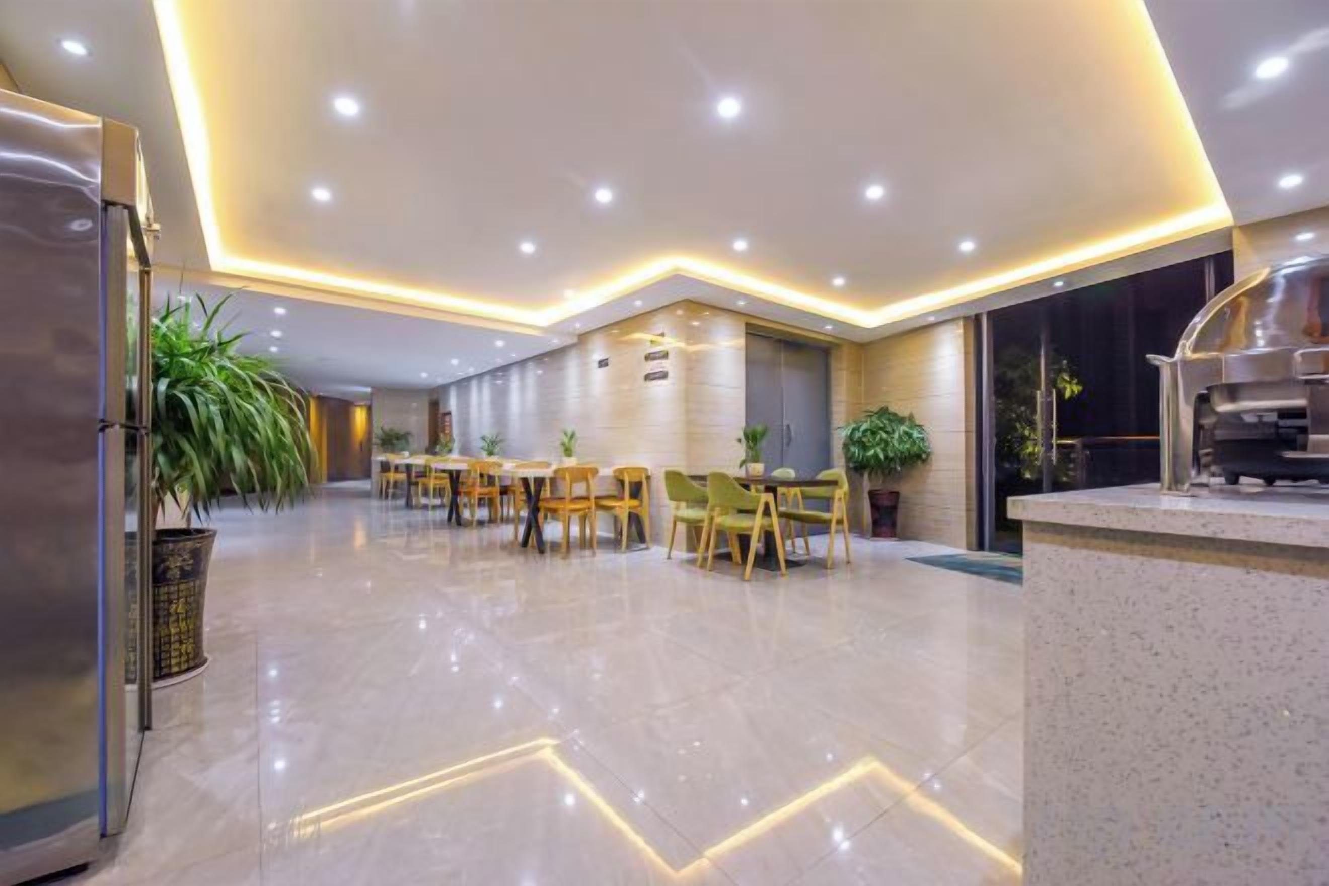 A modern hotel lobby with a dining area, a kitchen, and a reception desk.
