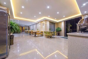 A modern hotel lobby with a dining area, a kitchen, and a reception desk.