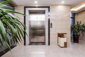 An elevator in a lobby with a marble floor, a potted plant, and a small wooden bench. - Chongqing Jinfeng Hotel (Chongqing)
