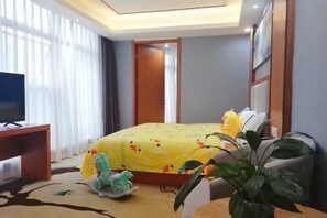 Quarto de hotel com cama, televisão, escrivaninha e planta em vaso.