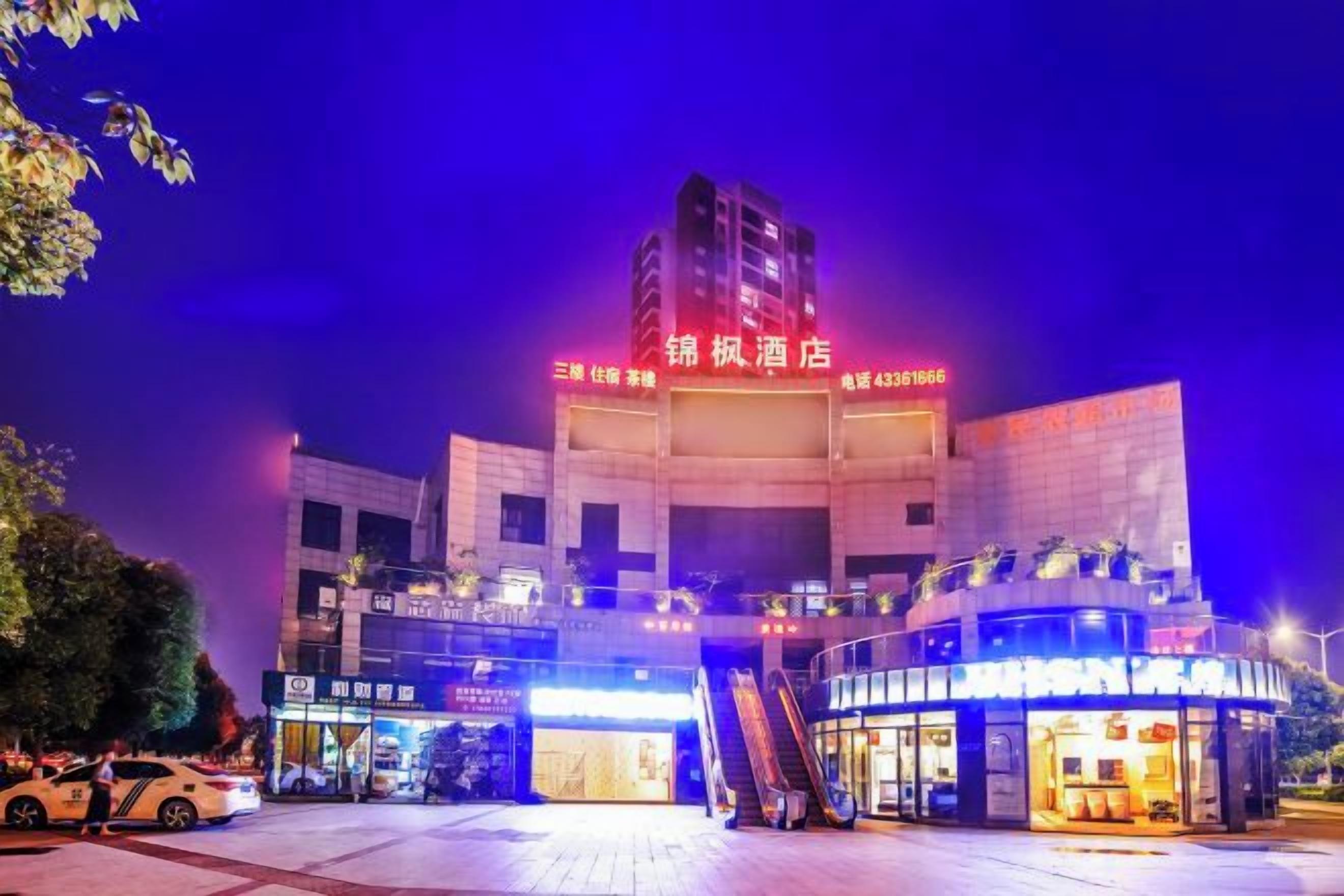 A hotel with a prominent sign, a covered entrance, and an adjacent building with illuminated signage.