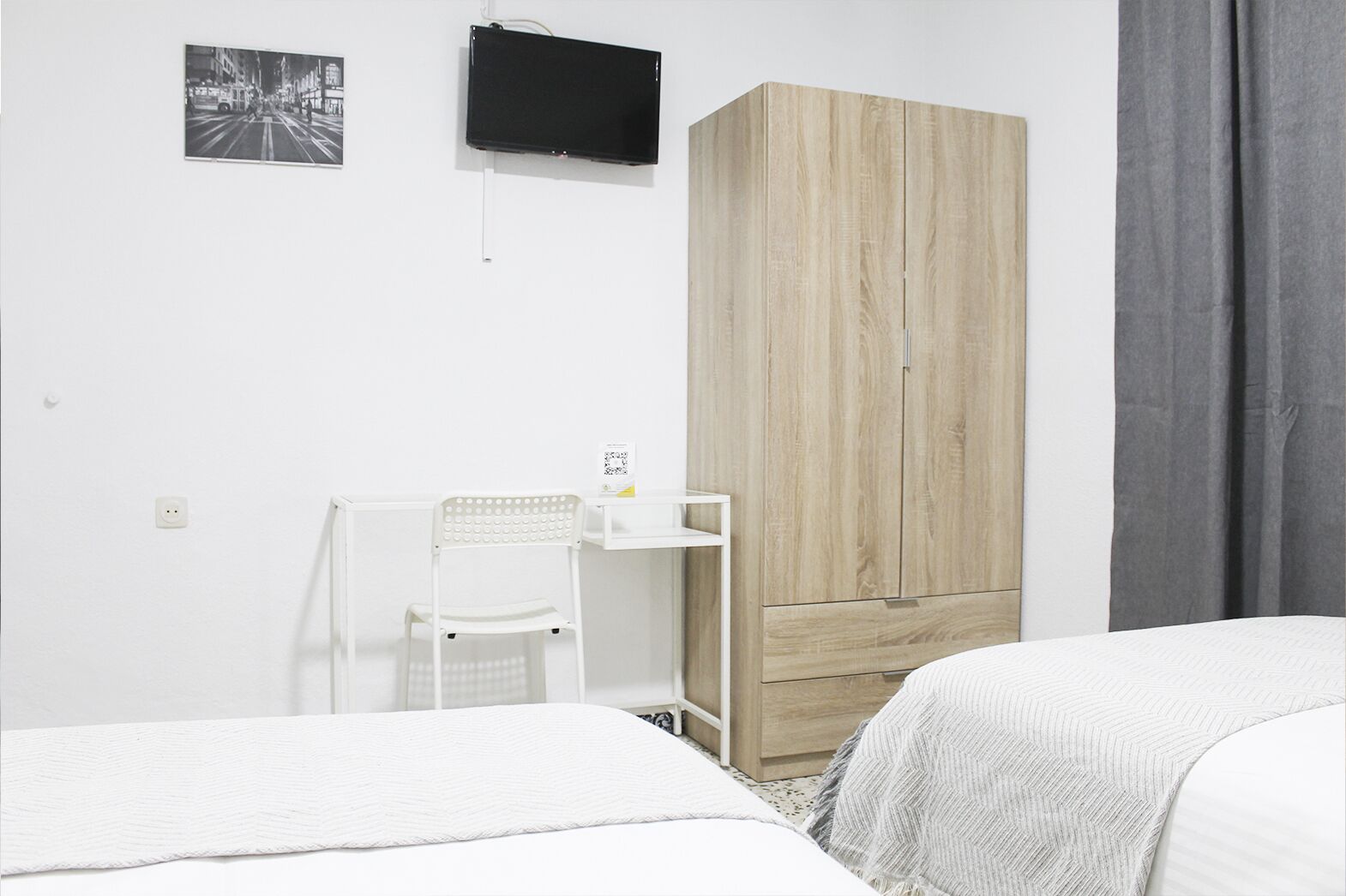 A bedroom with two beds, a desk with a chair, a wardrobe, and a television on the wall.
