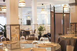 Un comedor con mesas redondas, cada una con cubiertos y copas de vino, e iluminación colgante.