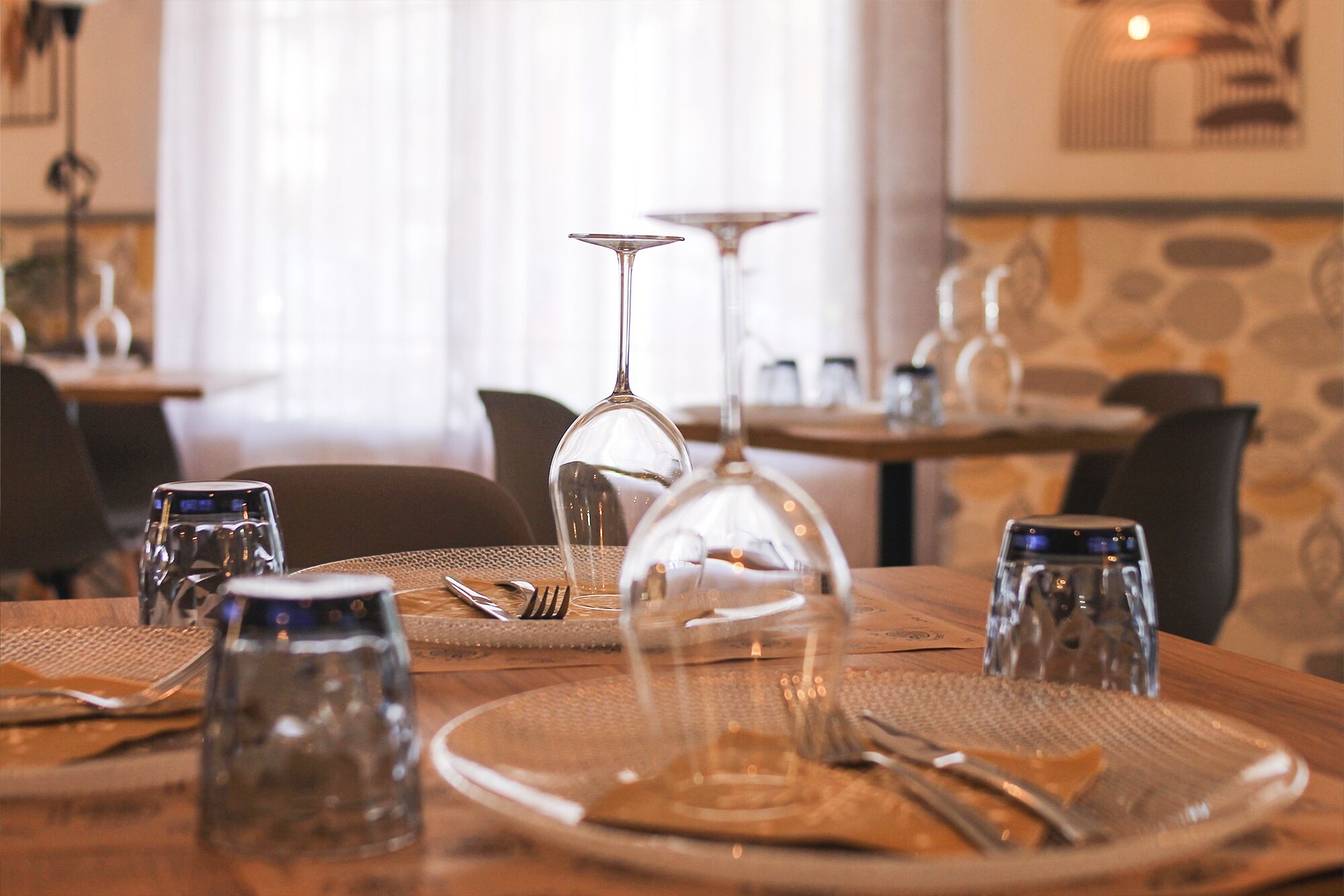 Una mesa de comedor dispuesta con cubiertos, vasos y una copa de vino.