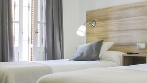 Een hotelkamer met twee bedden, een houten hoofdeinde, een nachtkastje en een raam met gordijnen.