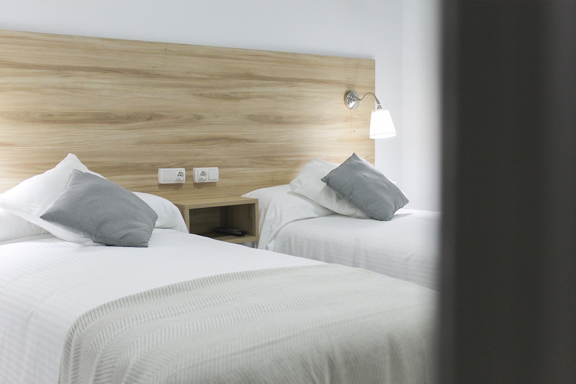A hotel room with two beds, a wooden headboard, bedside lamps, and a nightstand with a remote control.