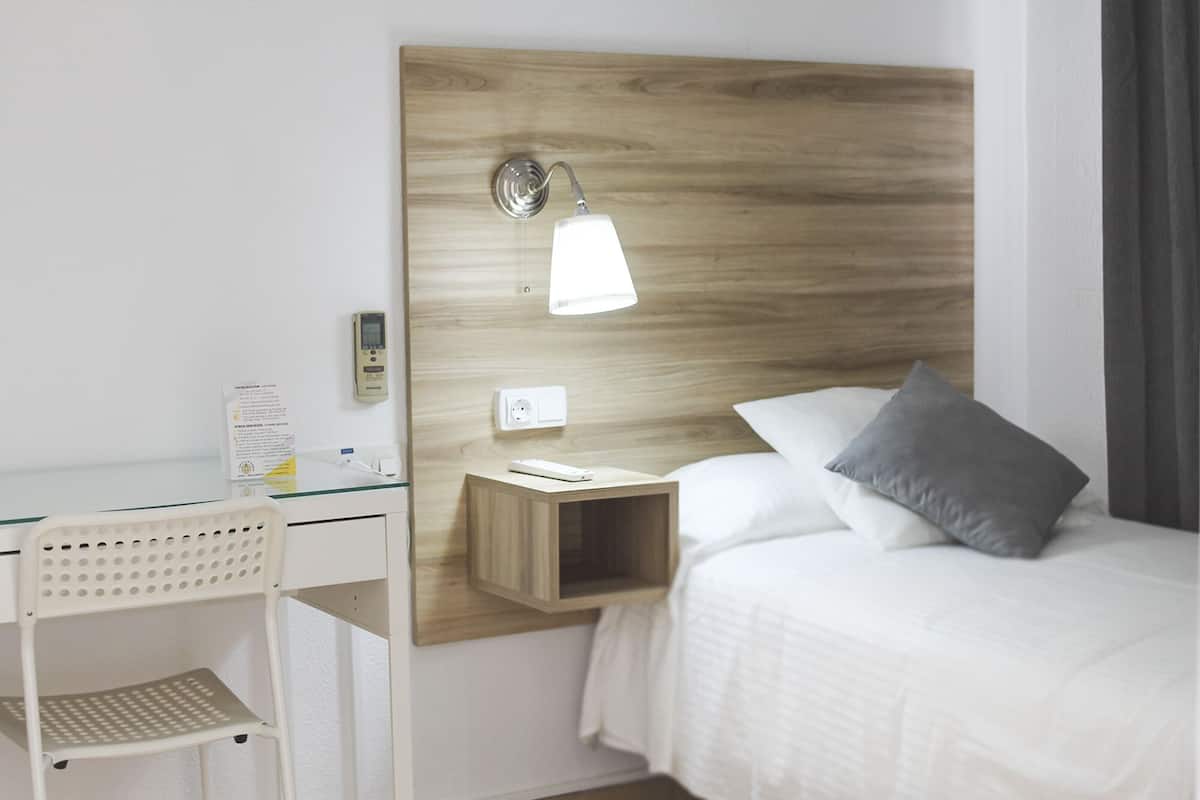 Une chambre d’hôtel avec une tête de lit en bois, une table de chevet avec une lampe, un bureau et une chaise.