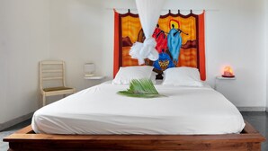 Un lit avec du linge de lit blanc, une tête de lit en bois, une table de chevet avec une lampe et une tapisserie colorée accrochée au mur.