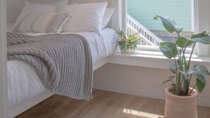 A bedroom with a bed, a window with a view of the sea, and a potted plant. - The Scenic Bunkalow | Walk to Beach + Bunk Room (Miramar Beach)