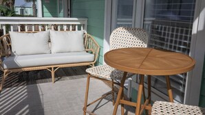 A wicker sofa with cushions, a round wooden table, and a woven chair on a wooden deck. - The Scenic Bunkalow | Walk to Beach + Bunk Room (Miramar Beach)