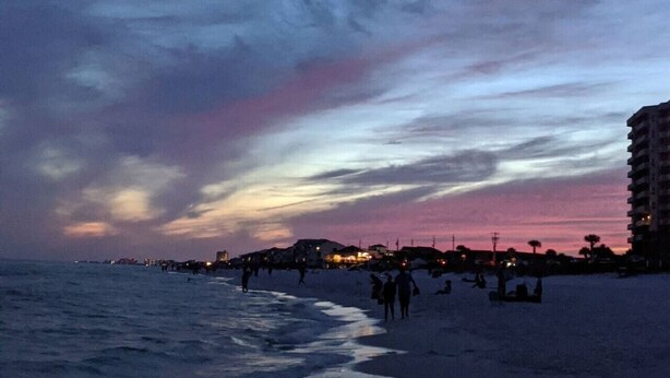 A beach at dusk with people walking along the shore and buildings in the background. - The Scenic Bunkalow | Walk to Beach + Bunk Room (Miramar Beach)