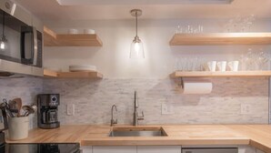A modern kitchen with a stainless steel sink, wooden countertops, a built-in oven, and a coffee machine. - The Scenic Bunkalow | Walk to Beach + Bunk Room (Miramar Beach)