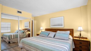 A bedroom with a bed, two bedside tables, a mirror, and a window with blinds.