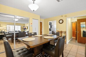 Un coin repas avec une table et des chaises en bois, une cuisine en arrière-plan et un couloir menant à une porte.