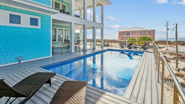 A modern pool area with a wooden deck, lounge chairs, and a view of the beach and ocean.