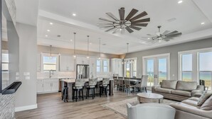 A spacious living area with a large sofa, a dining table with chairs, and a kitchen area with white cabinets and a central island.