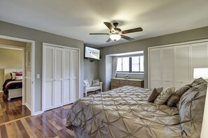 A bedroom with a bed, a ceiling fan, a TV, and a window.