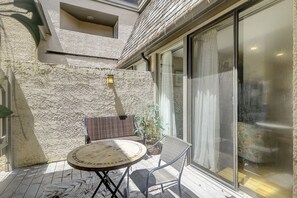 A patio with a round table and two chairs, a textured wall, a lantern, and a sliding glass door.