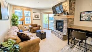 A modern living room with a stone fireplace, leather sofa, and a dining area with bar stools. - Near Bike Park, Dining, Shops! Outdoor Hot Tubs! (Keystone)