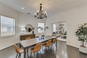 A spacious dining area with a long table, multiple chairs, a chandelier, and a potted plant.
