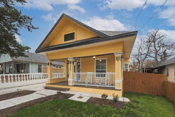 A two-story house with a front porch, a fenced backyard, and a clear sky.