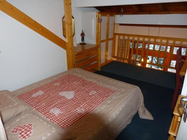 A bedroom with a bed, a wooden dresser, and a window with a view of a snowy landscape.